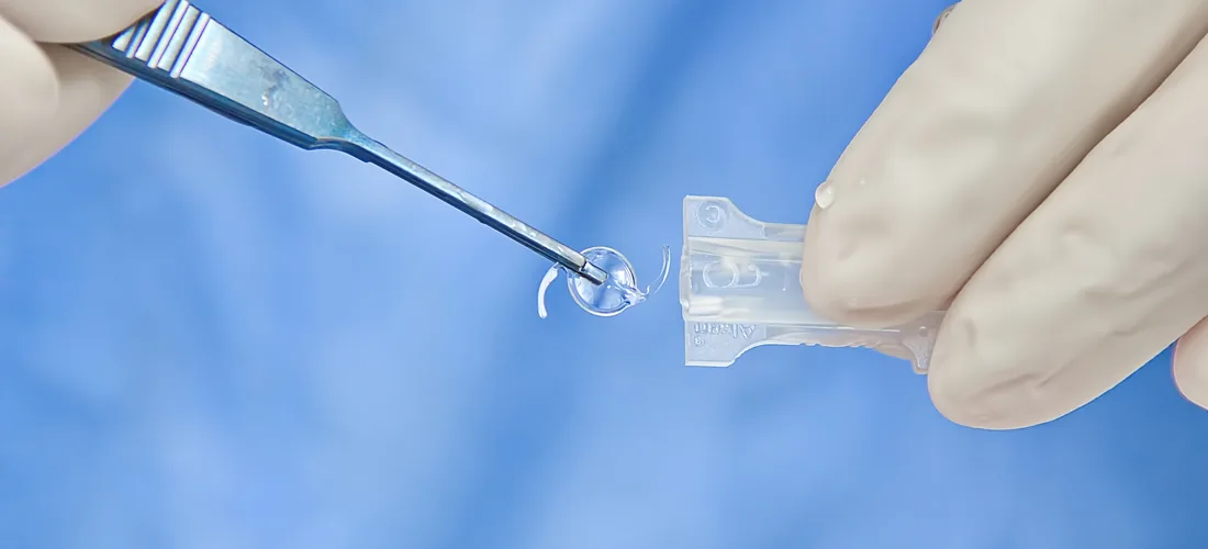 An intraocular lens held on forceps in front of a patient’s eye