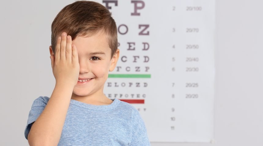 A young boy covering one eye during a vision test in front of an eye chart