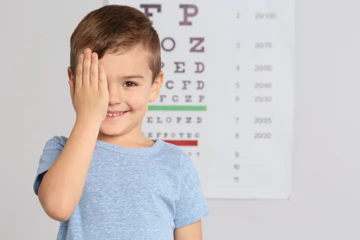 A young boy covering one eye during a vision test in front of an eye chart